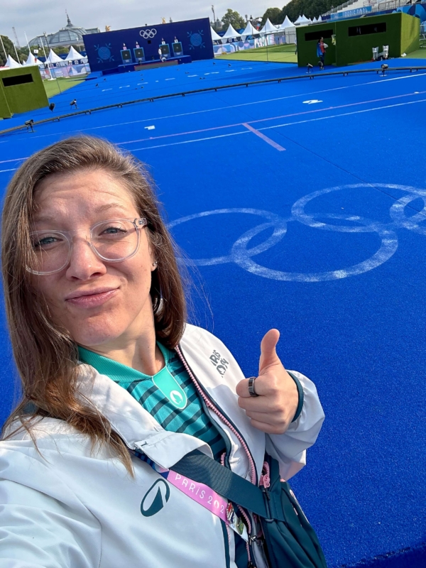 Jordan posing for a selfie in her olympic volunteer uniform. She is standing on the archery field in the days before the games.